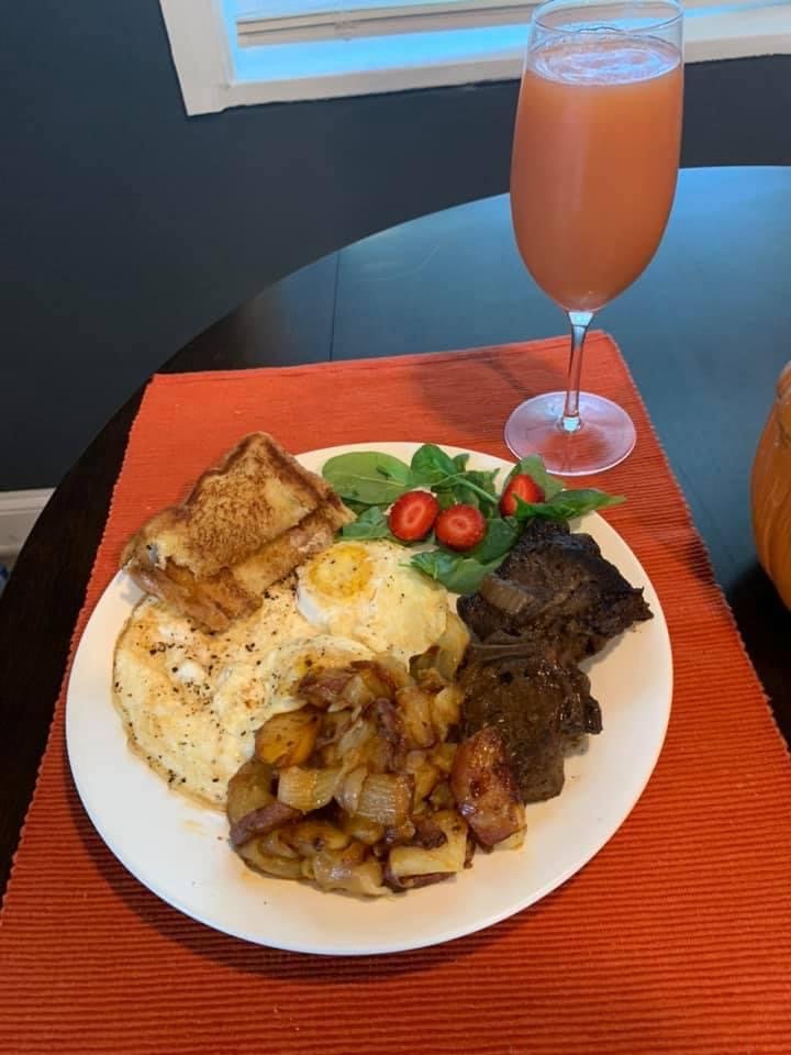 A breakfast plate with fried eggs, fried potatoes, steak, grilled toast, and a small side salad with strawberries, next to a glass of pink juice