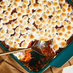 Sweet potato casserole topped with toasted miniature marshmallows in a teal baking dish